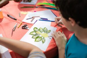 Kinder basteln bei Sommerfest-Aktivität mit bunten Stiften, Papier und Blättern