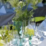 Moderne Sommerdeko mit Disteln, Grünpflanzen und Gläsern auf dem gedeckten Tisch