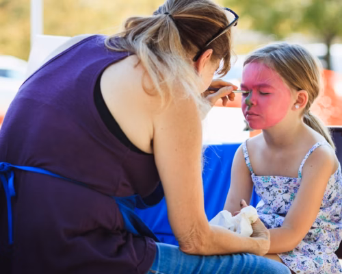 Kinderprogramm mit Schminkecke – Spaß für die kleinen Gäste Frau schminkt Mädchen mit pinkem Gesicht beim Kinderschminken